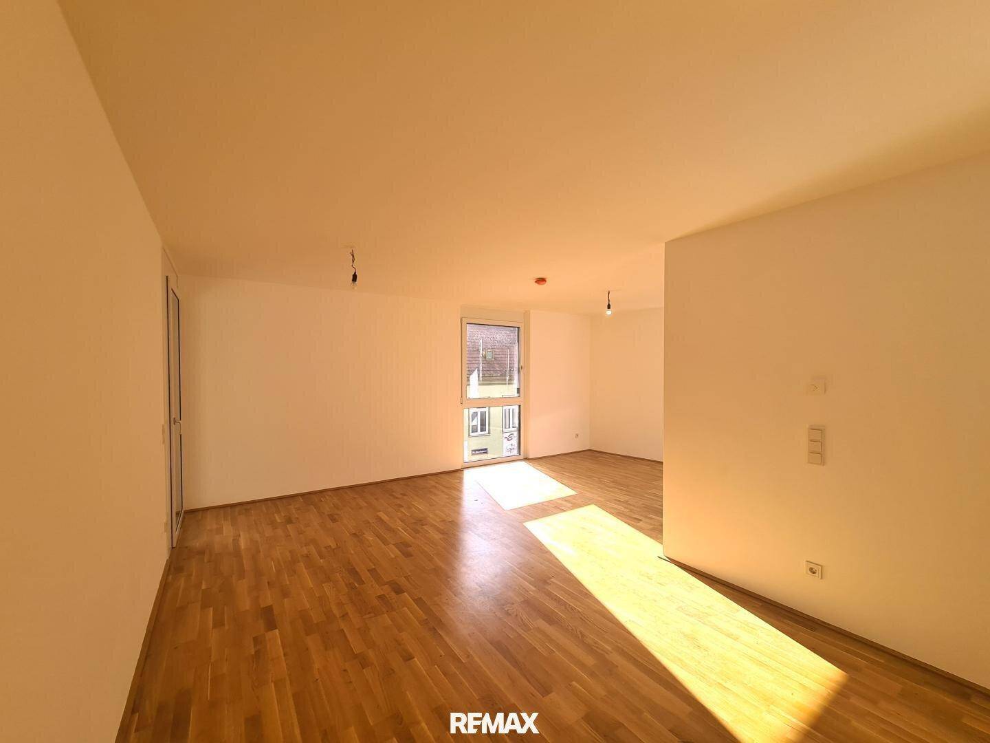 Heller Raum mit Holzboden und Fenster, das Sonnenlicht auf den Boden wirft, ideal als Wohnbereich.