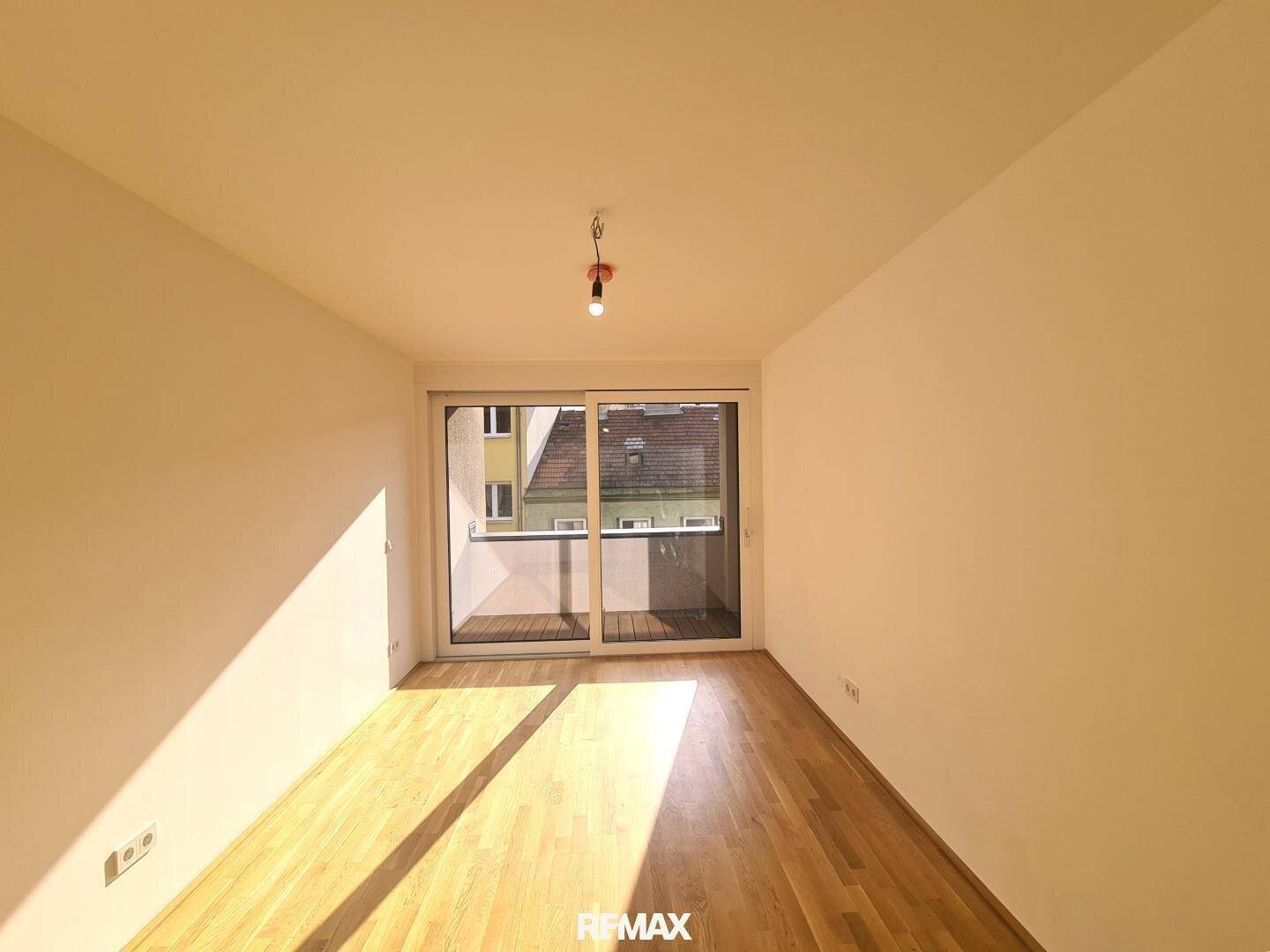 Heller Raum mit Parkettboden und großen Schiebetüren, die auf einen kleinen Balkon führen.