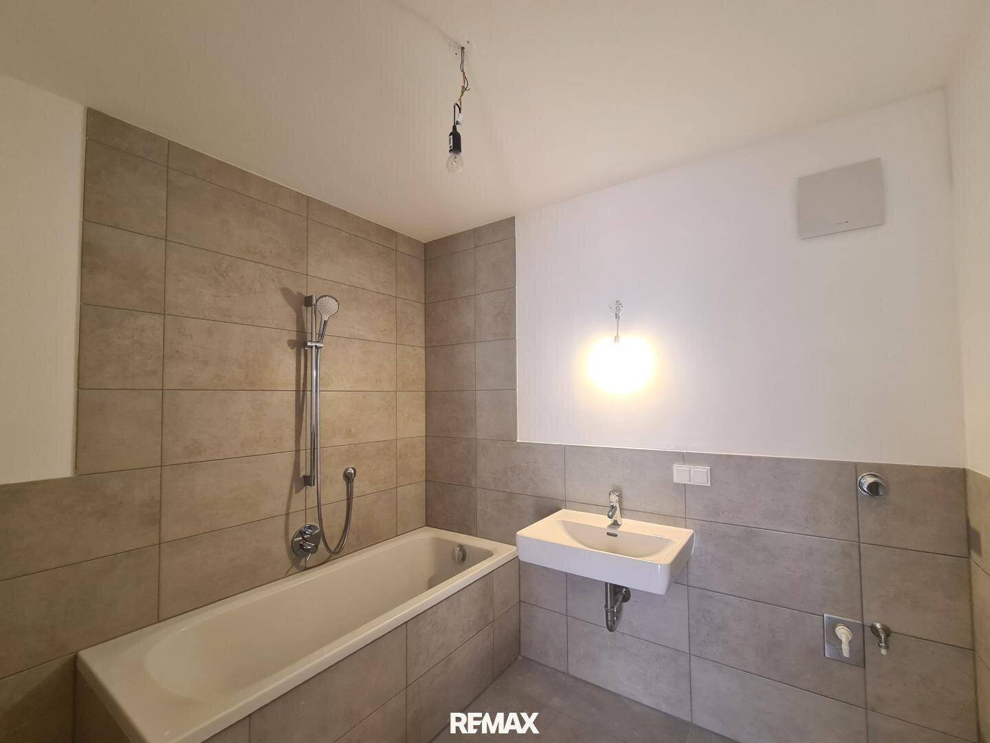 Modernes Badezimmer mit Badewanne, Waschbecken und beigefarbenen Fliesen an den Wänden.