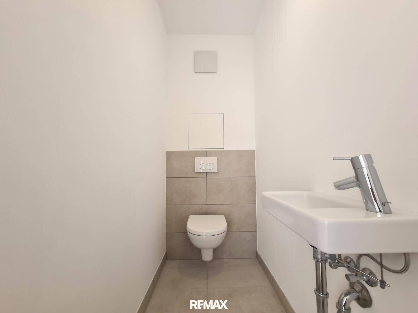 Separates Gäste-WC mit wandhängender Toilette, kleinem Waschbecken und Fliesen.