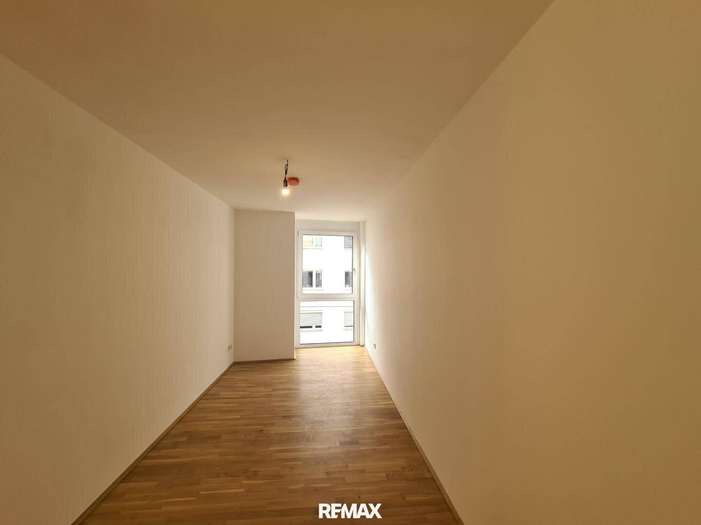 Langes, schmales Zimmer mit Parkettboden und einem Fenster am Ende, ideal als Schlafzimmer.