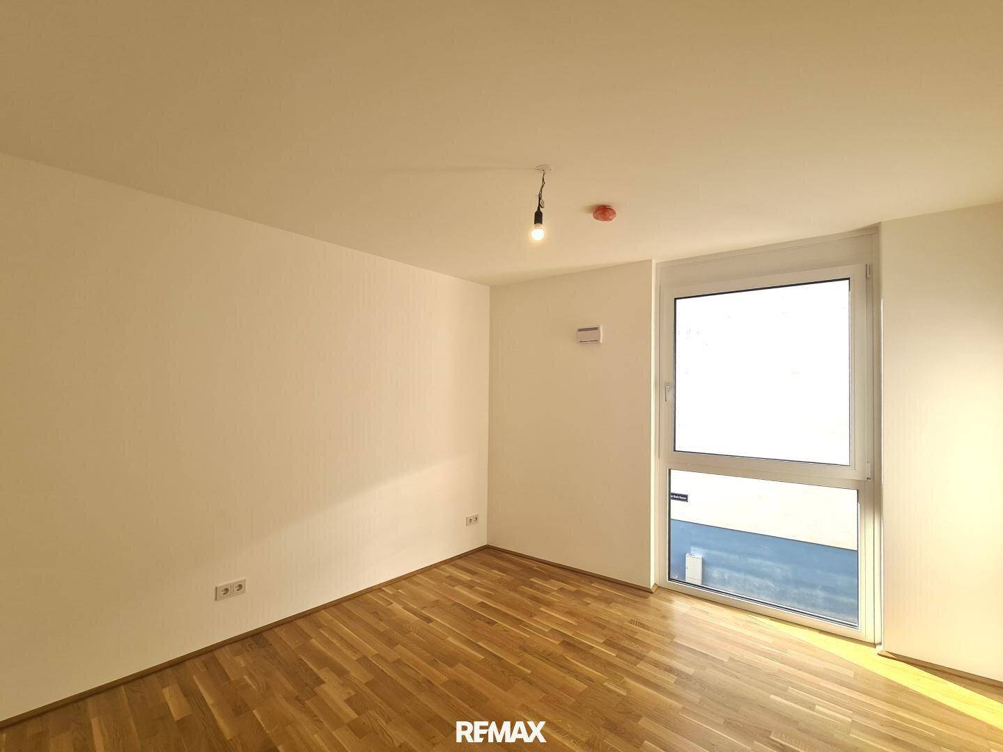 Helles Zimmer mit Parkettboden und einem großen Fenster, das den Raum gut belichtet.