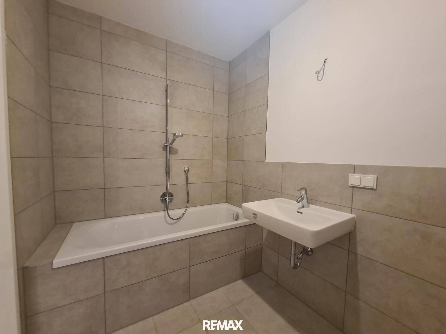 Modernes Badezimmer mit beigefarbenen Fliesen, Badewanne mit Duschfunktion und Einzelwaschbecken.