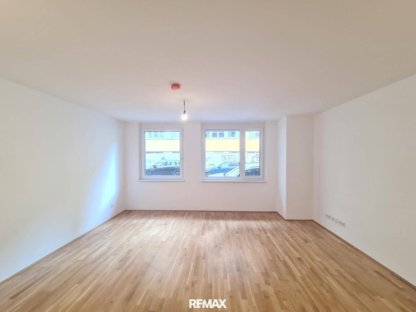 Lichtdurchfluteter Raum mit hellem Parkettboden und großen Fenstern, ideal als Wohnbereich.