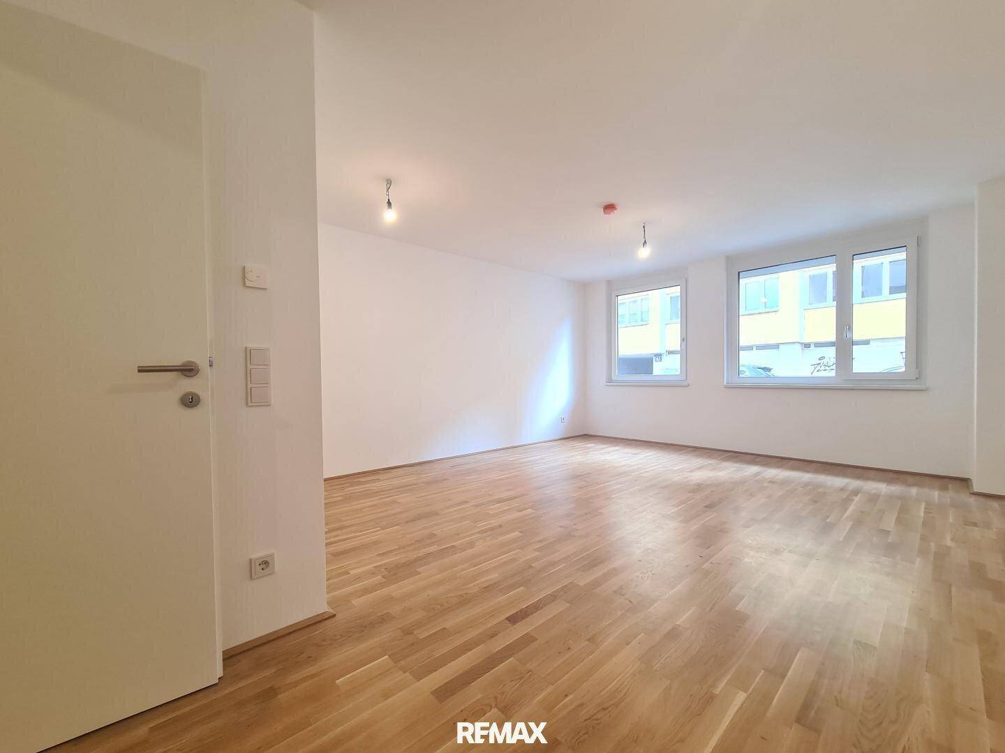 Helles, leeres Wohnzimmer mit neuem Parkettboden und großen Fenstern, bereit zur Einrichtung.