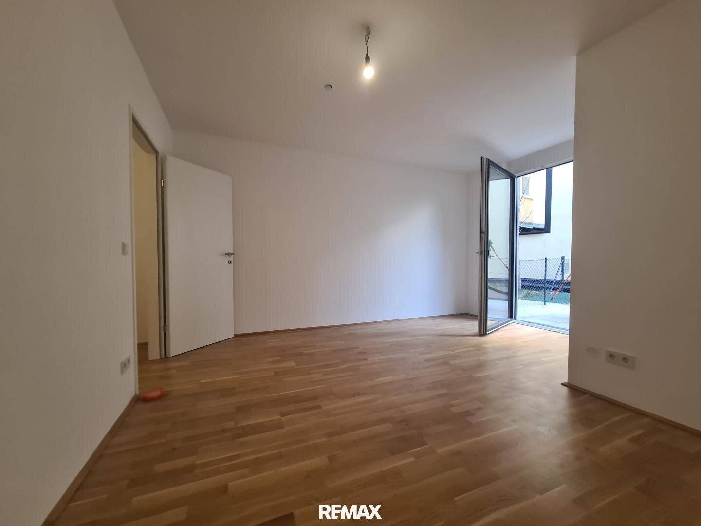 Geräumiges Wohnzimmer mit hellem Parkettboden und direktem Zugang zur Außenterrasse.