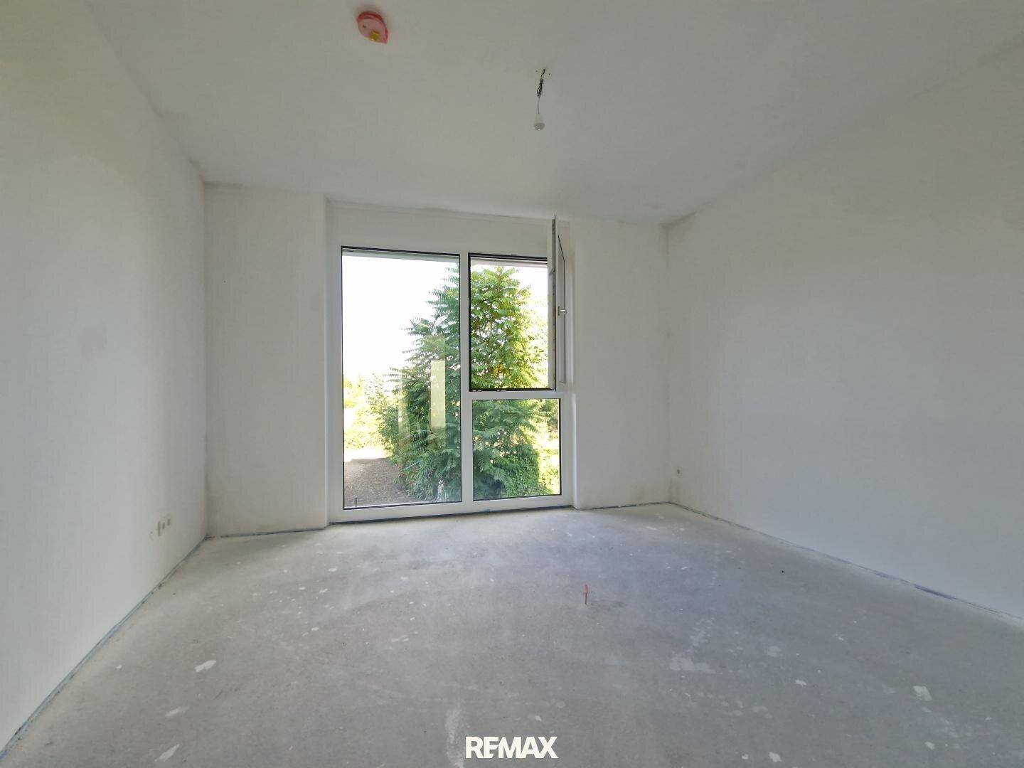 Heller, unfertiger Raum mit großem Fenster und Blick auf Bäume, ideal als Schlafzimmer oder Büro.