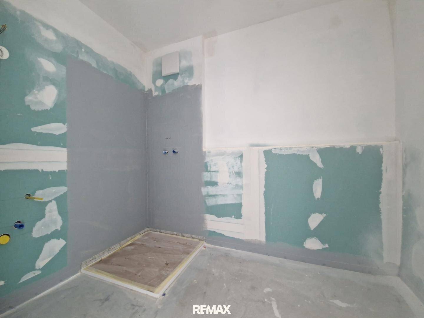 Badezimmer im Rohbau mit vorbereiteter Duschfläche und Installationen für Sanitäranlagen.