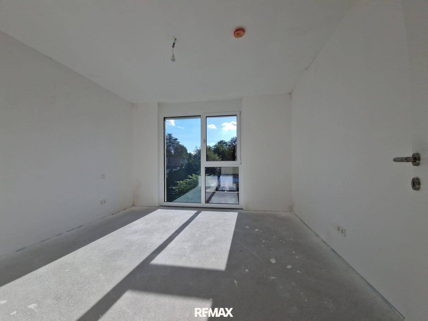 Geräumiger, unfertiger Innenraum mit viel Tageslicht durch eine große Fenstertür, bereit für den Ausbau.
