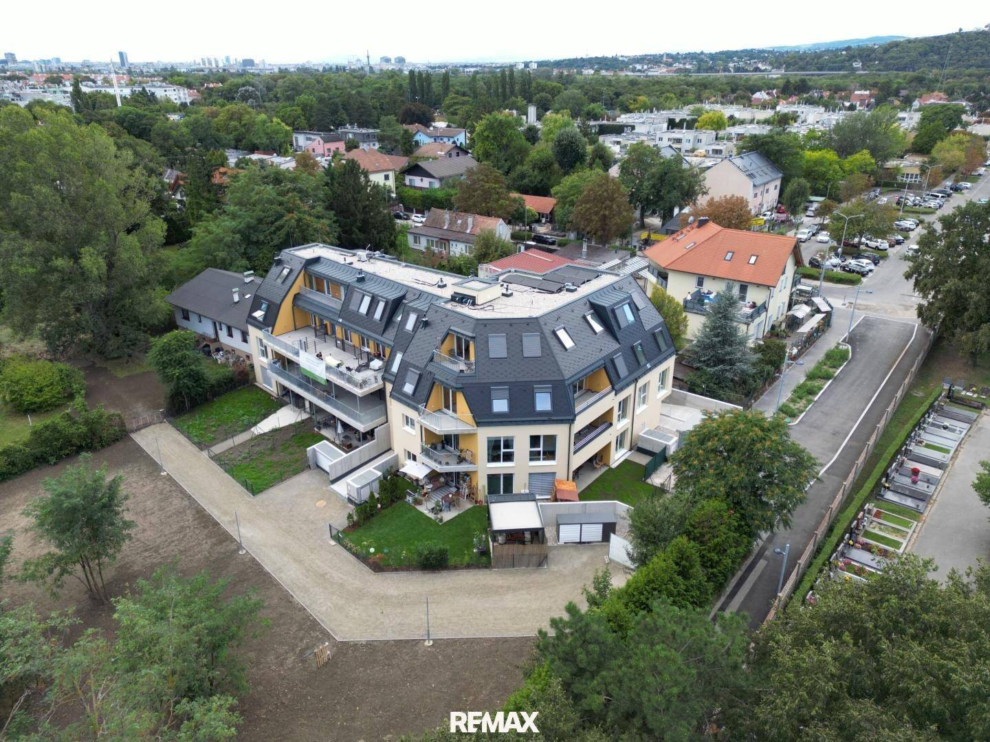 Panoramablick auf das moderne Wohngebäude mit umliegenden Grünflächen und städtischer Bebauung im Hintergrund.