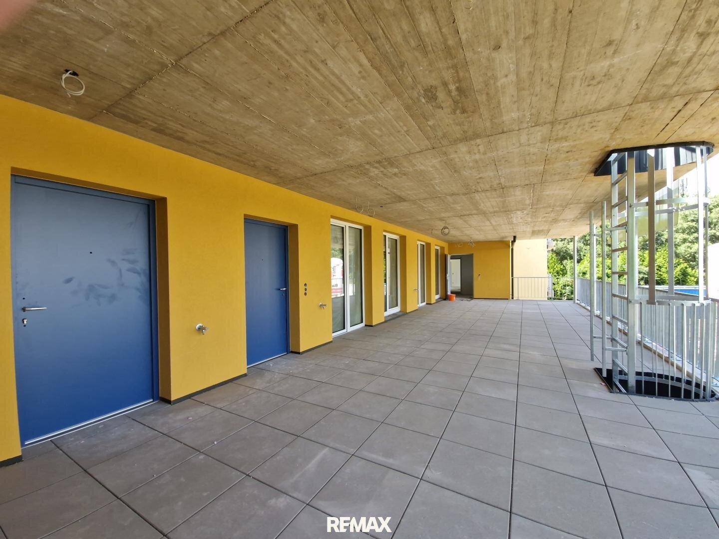 Weitläufige, überdachte Terrasse mit mehreren Zugängen zu den Wohneinheiten und Blick ins Grüne.