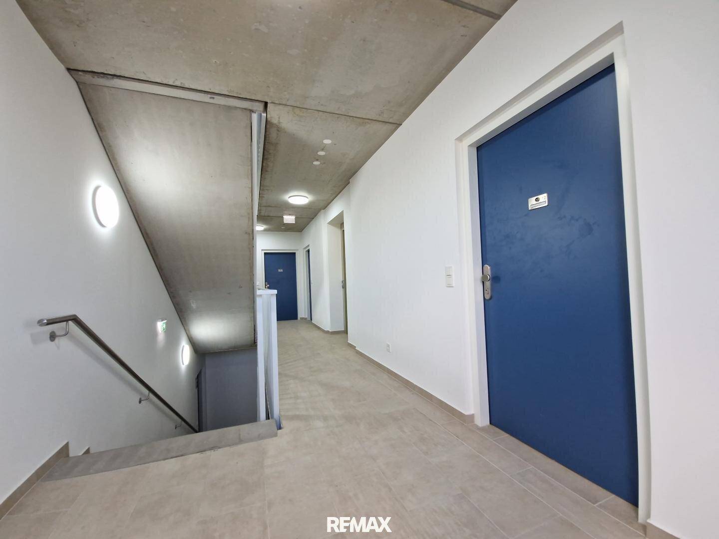 Moderner Flur mit Treppenhaus und blauen Wohnungstüren, bietet Zugang zu den Etagen.