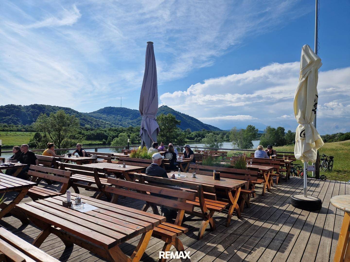 Gemütlicher Außenbereich eines Restaurants mit Holztischen und Bänken, Blick auf den Fluss.