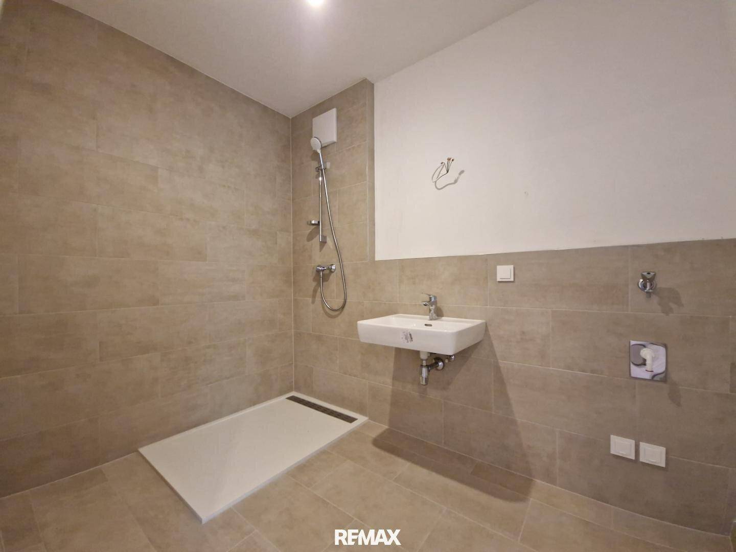 Modernes Badezimmer mit beigefarbenen Fliesen, ebenerdiger Dusche und Einzelwaschbecken.