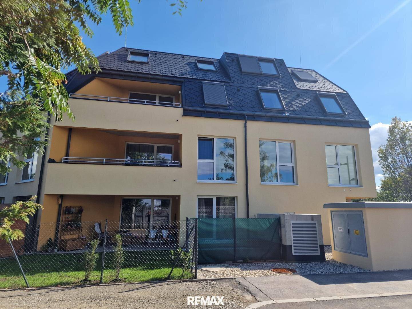 Modernes Mehrfamilienhaus mit gelber Fassade, Balkonen und Dachfenstern in grüner Umgebung.