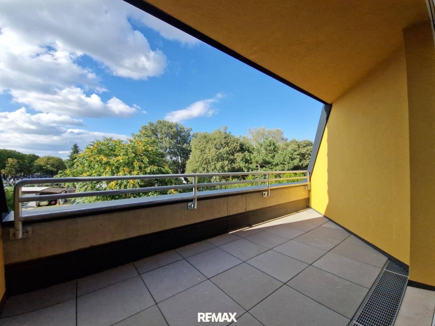 Geräumiger Balkon mit Fliesenboden und Metallgeländer, bietet einen schönen Ausblick ins Grüne.