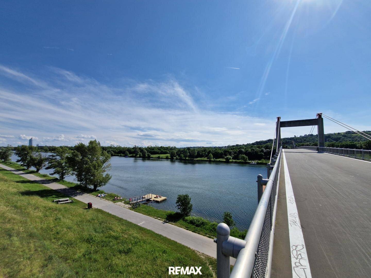 Malerischer Blick auf einen Fluss mit Brücke und grünen Ufern unter blauem Himmel.