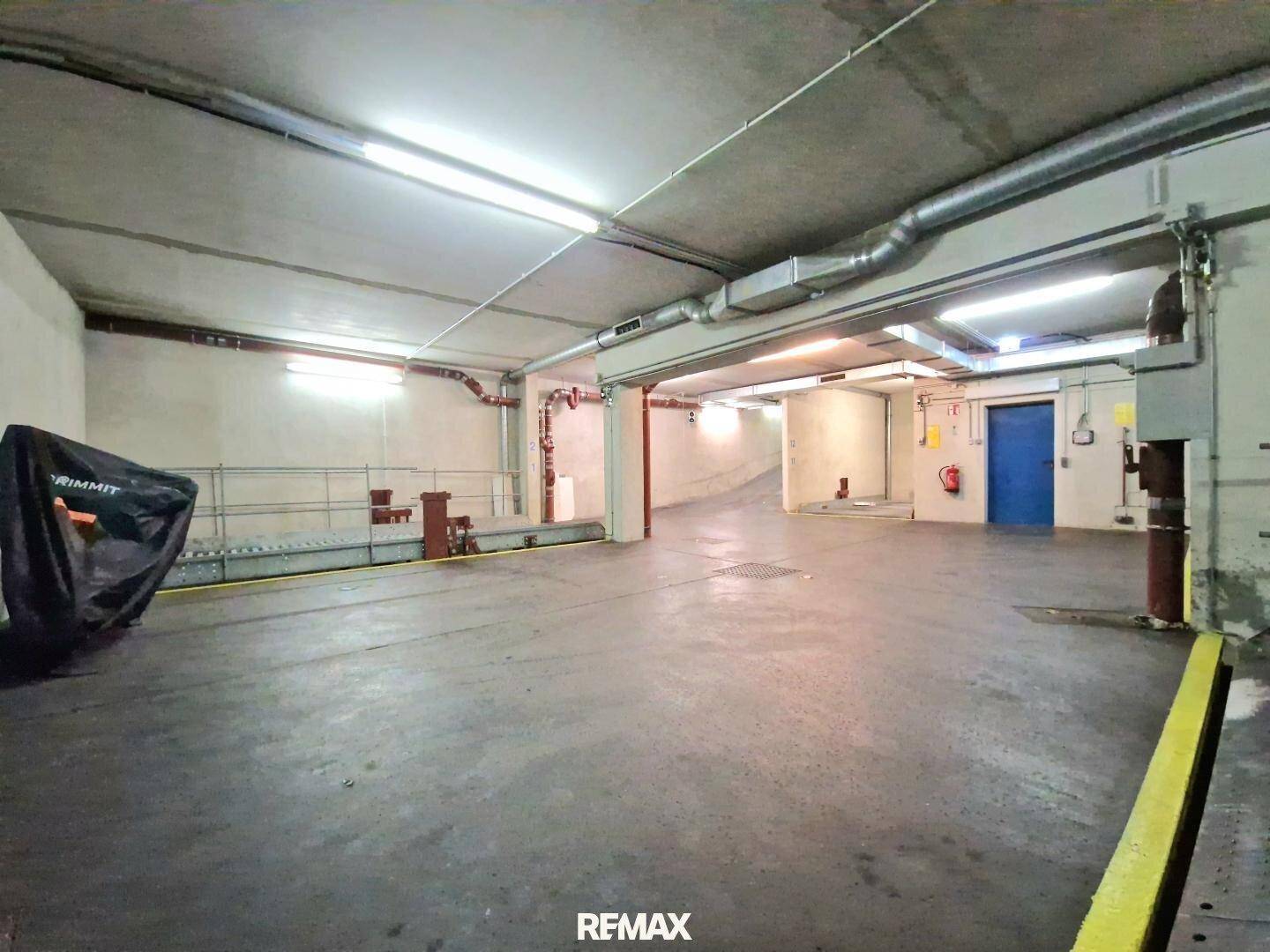 Weitläufige Tiefgarage mit Zufahrtsrampe und Parkplätzen, gut beleuchtet.