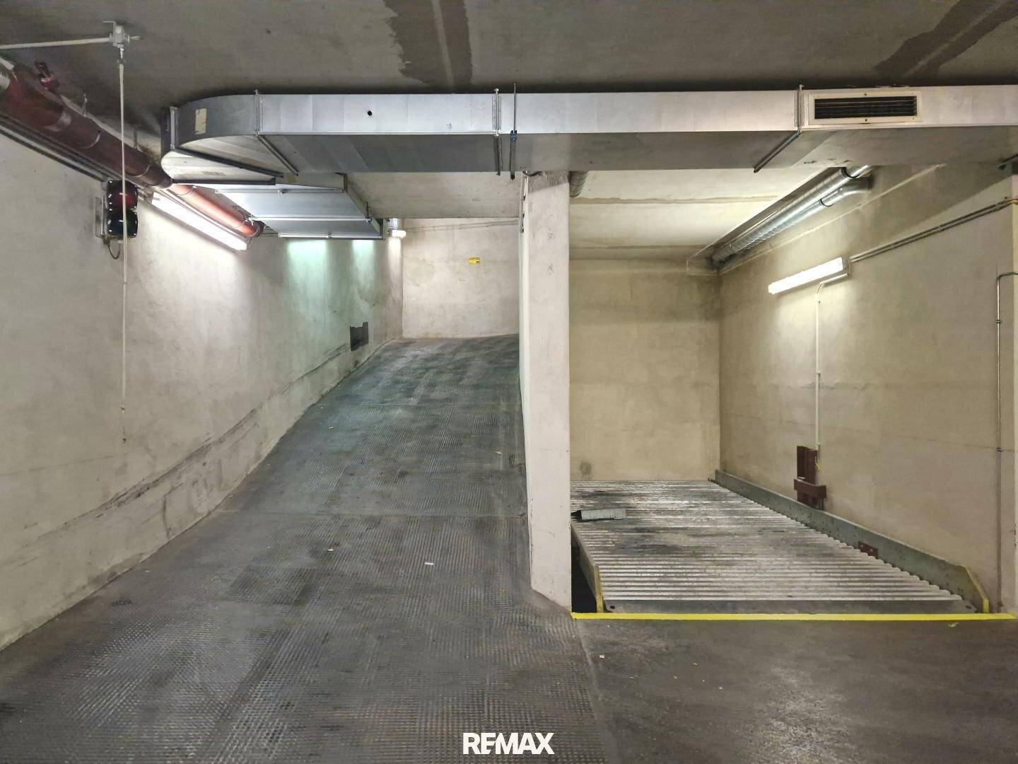 Zufahrtsrampe in der Tiefgarage mit Betonwänden und Lüftungsrohren, daneben ein Doppelparker.