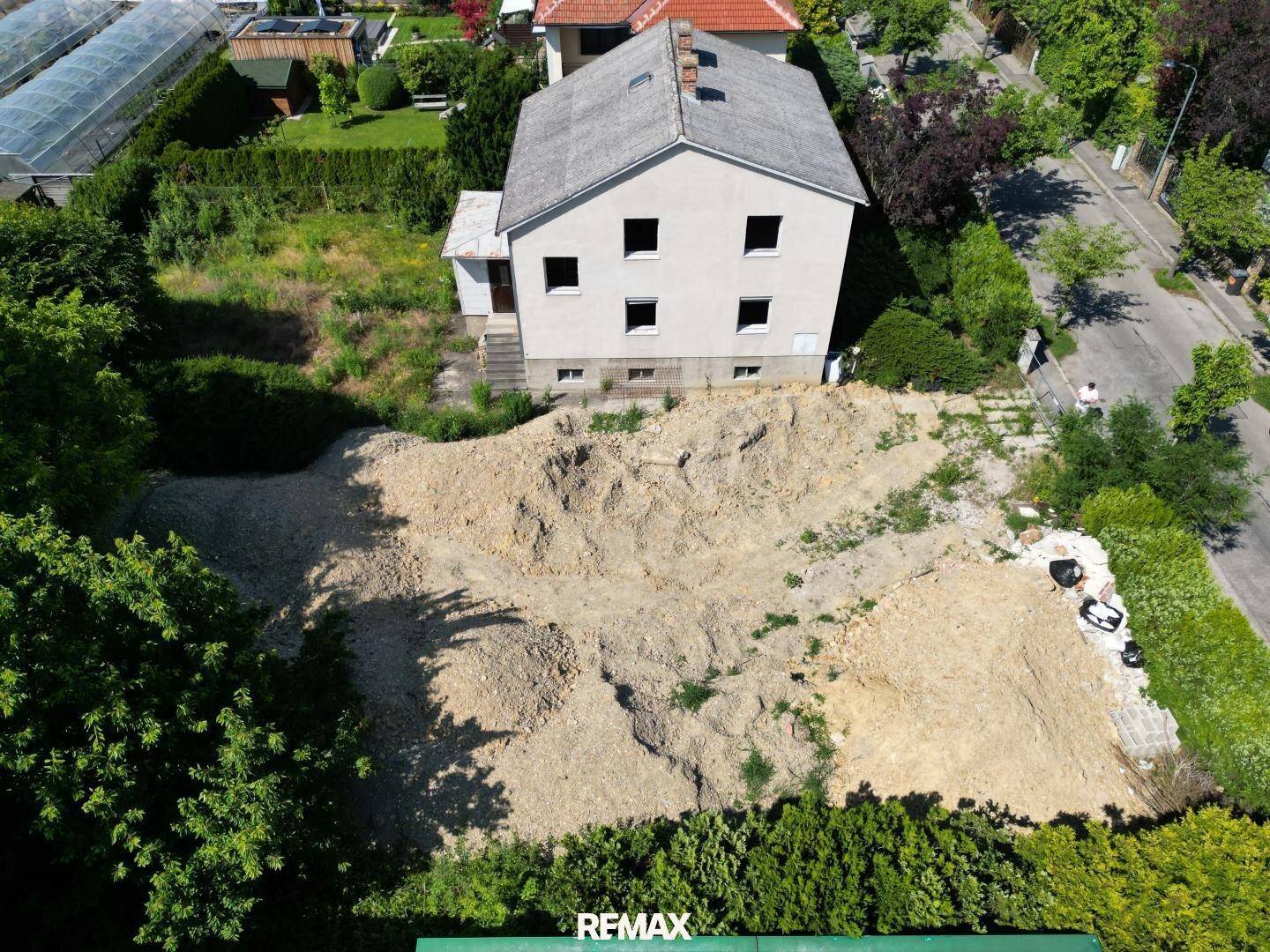 Luftaufnahme eines Grundstücks mit Bestandsgebäude und vorbereiteter Baufläche für Neubau.