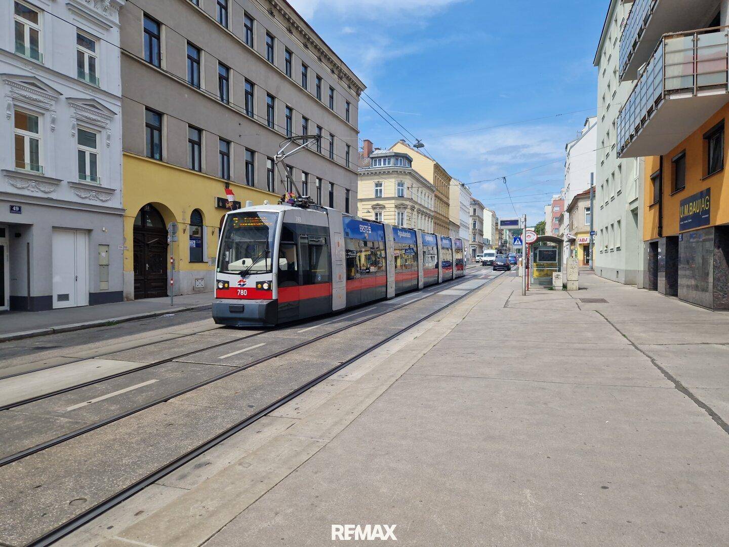Straßenansicht mit einer Straßenbahn auf den Gleisen und städtischer Bebauung.