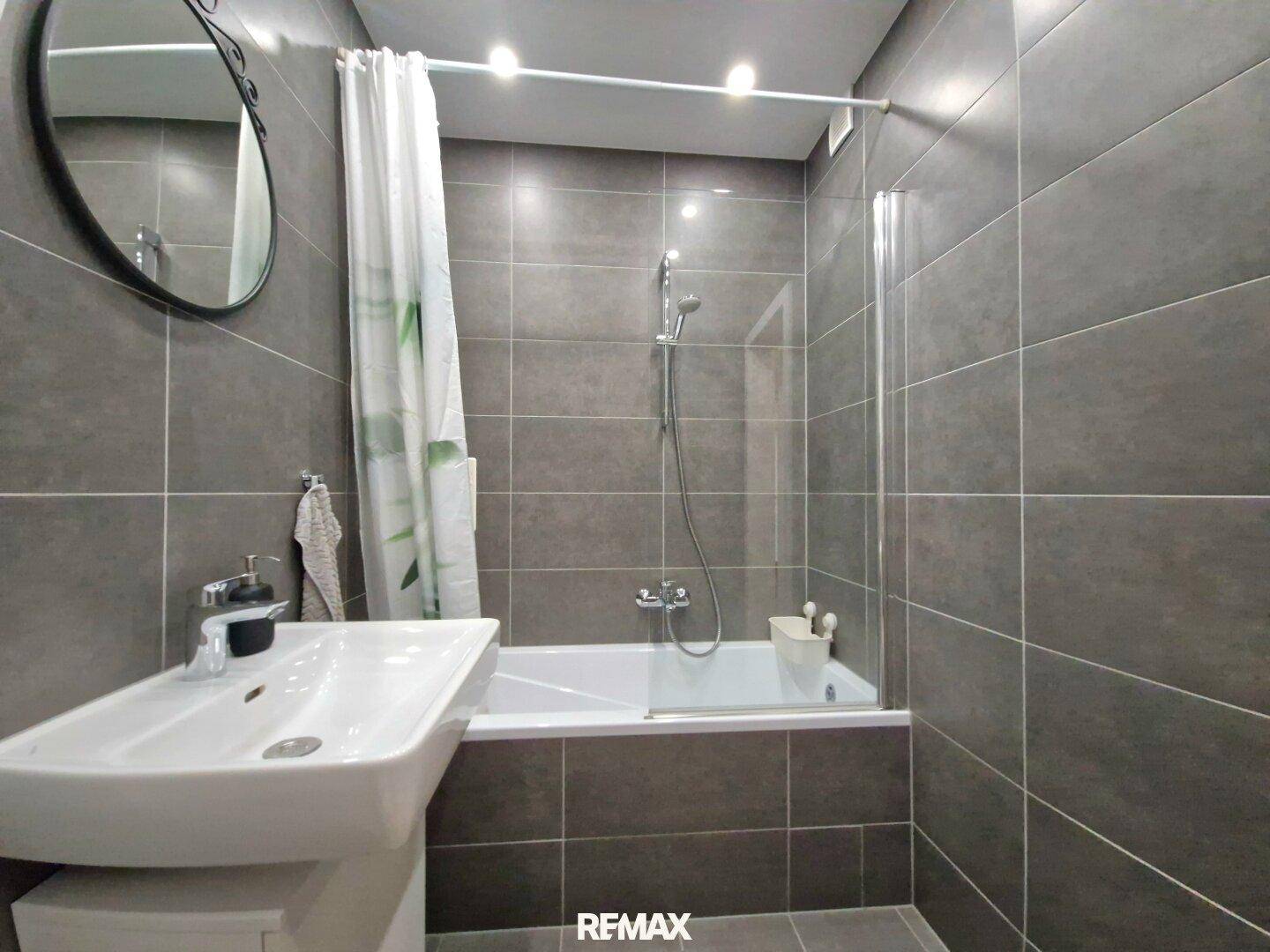 Badezimmer mit Badewanne inklusive Duschfunktion und modernem Waschbecken.