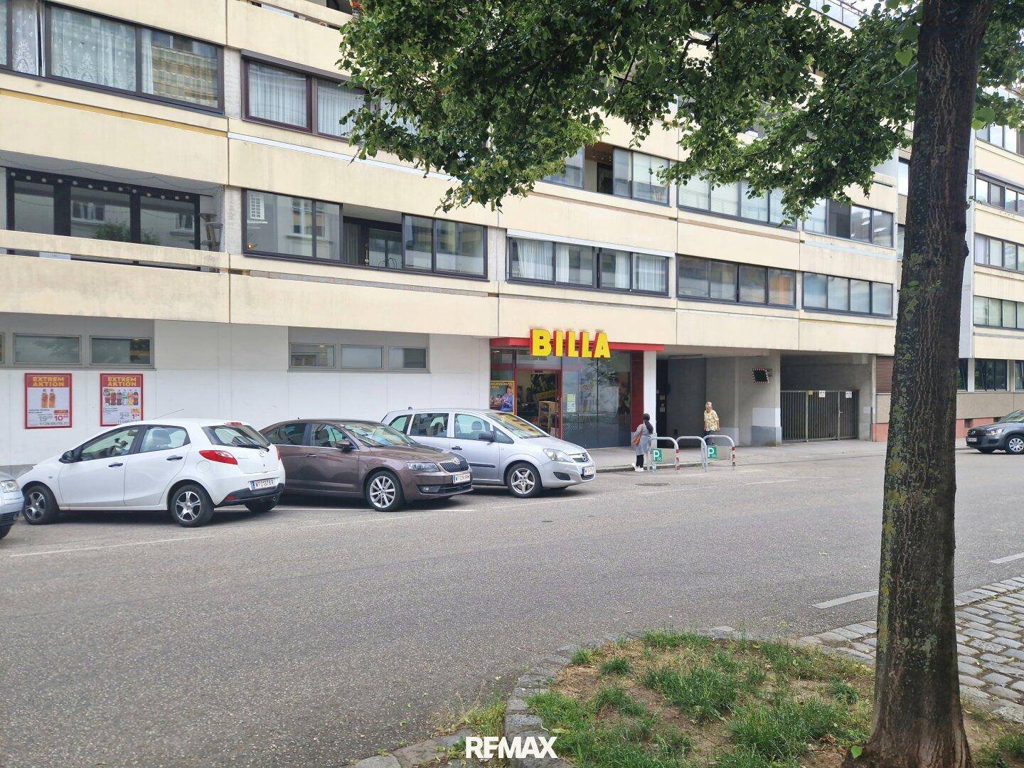 Gebäude mit Supermarkt im Erdgeschoss und Parkplätzen davor.
