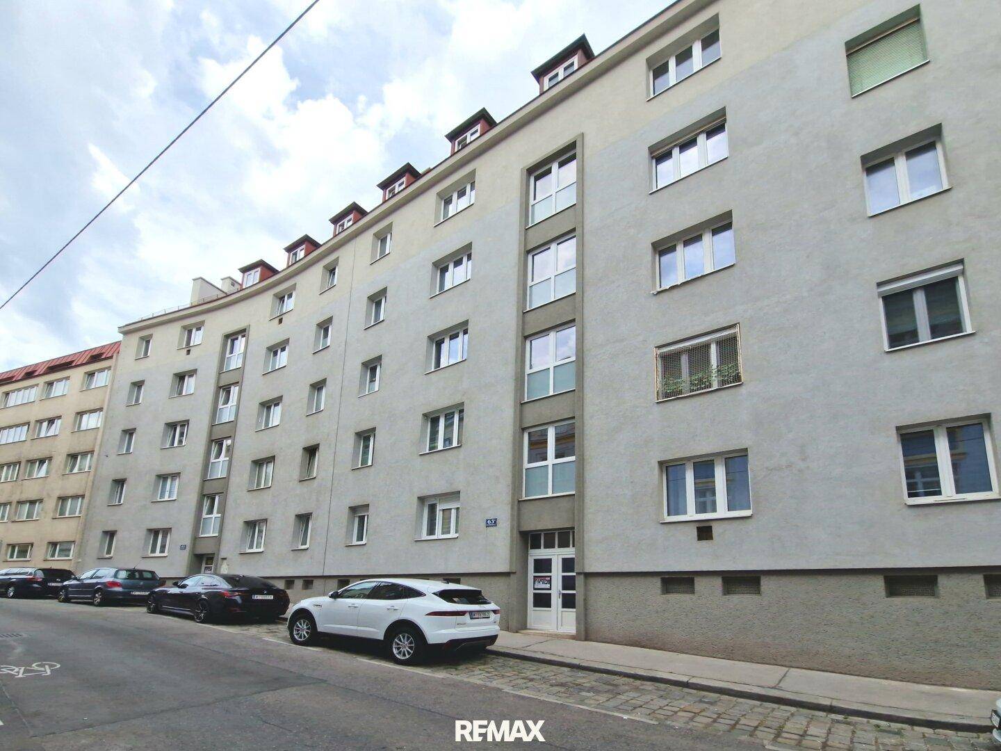Ansicht des Mehrfamilienhauses von der Straße mit parkenden Autos.