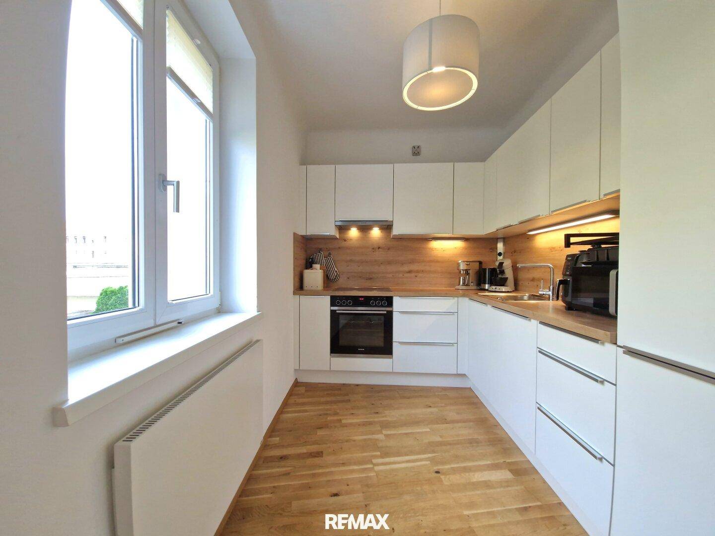 Moderne Küche mit weißen Schränken, Holz-Arbeitsplatte und Fenster für natürliches Licht.
