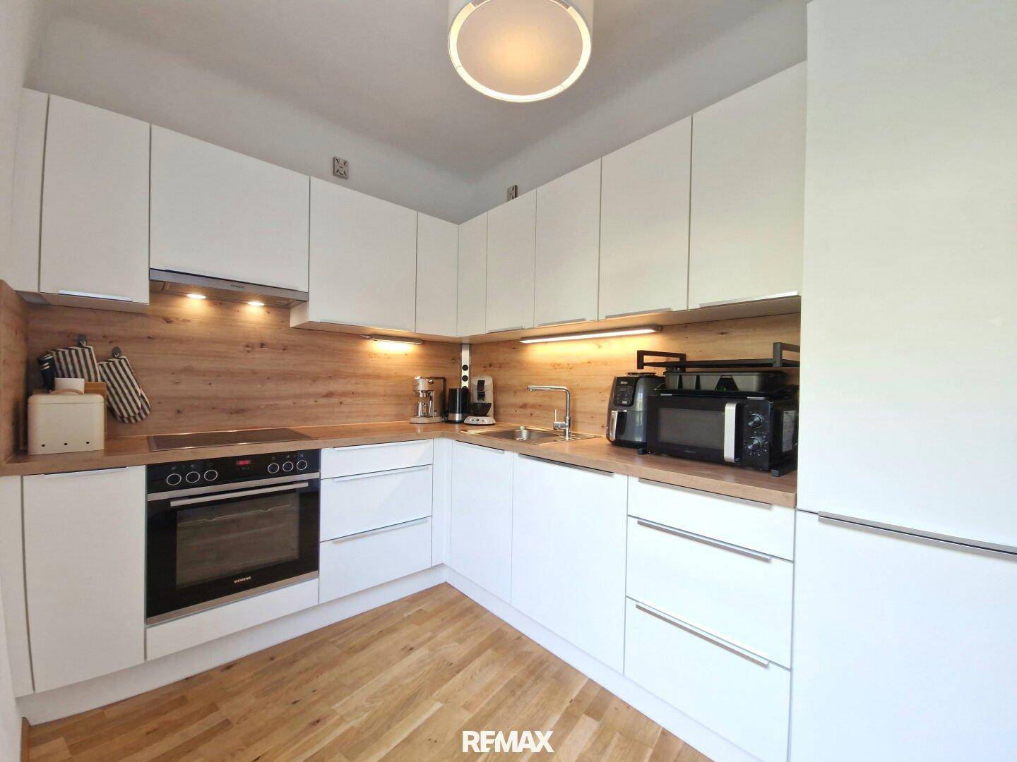 Funktionale Küche mit weißen Schränken, Holz-Arbeitsplatte und modernen Geräten.
