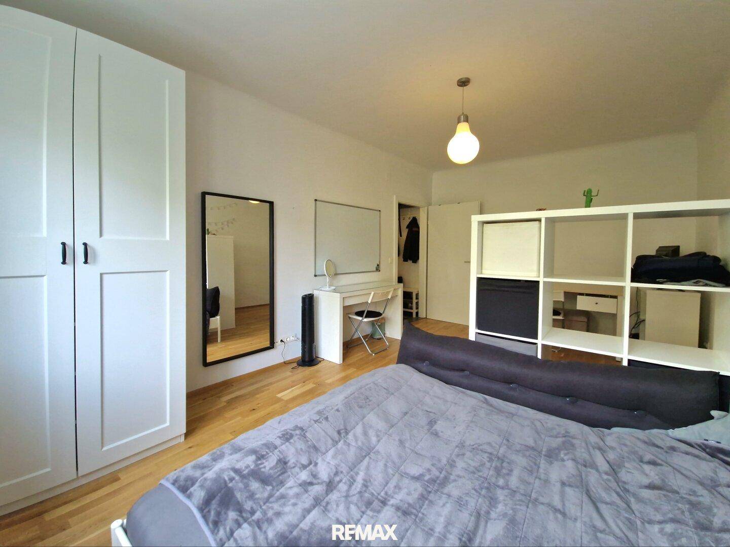 Schlafzimmer mit großem Kleiderschrank, Spiegel und hellem Holzfußboden.