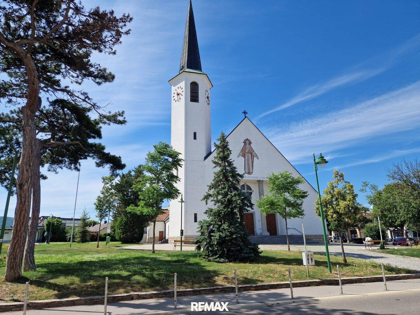Historische Kirche mit hohem Turm und grüner Parkanlage an einem sonnigen Tag.