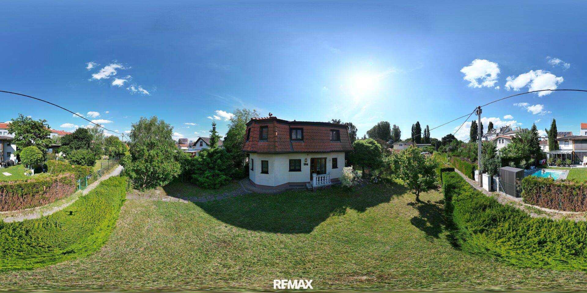 Weitläufiger Garten mit Einfamilienhaus, viel Grünfläche und sonnigem Himmel.