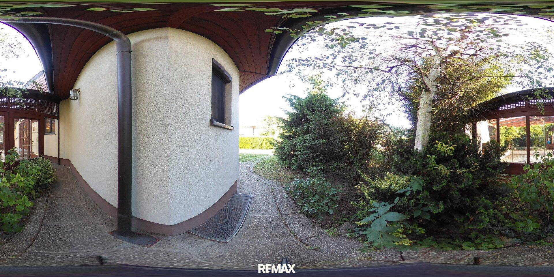 Seitenansicht des Hauses mit geschwungener Fassade und umgebender Bepflanzung.