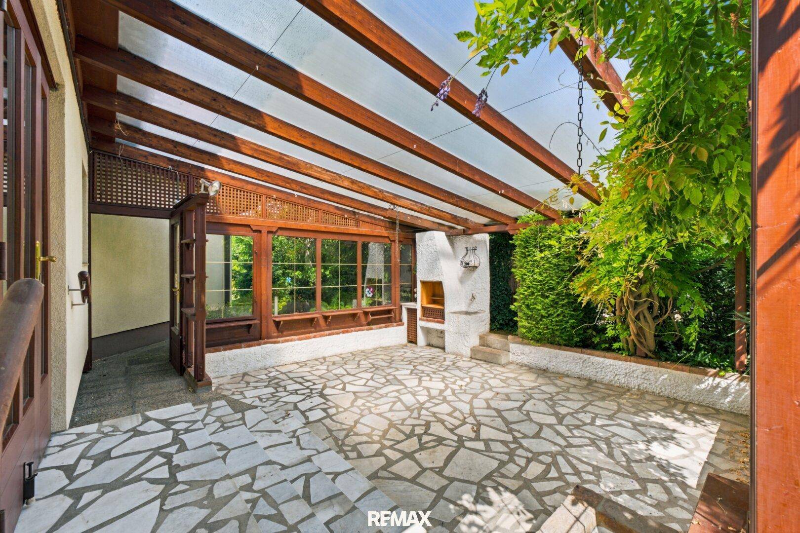 Geräumige überdachte Terrasse mit Mosaikboden, integriertem Grill und Blick ins Grüne.