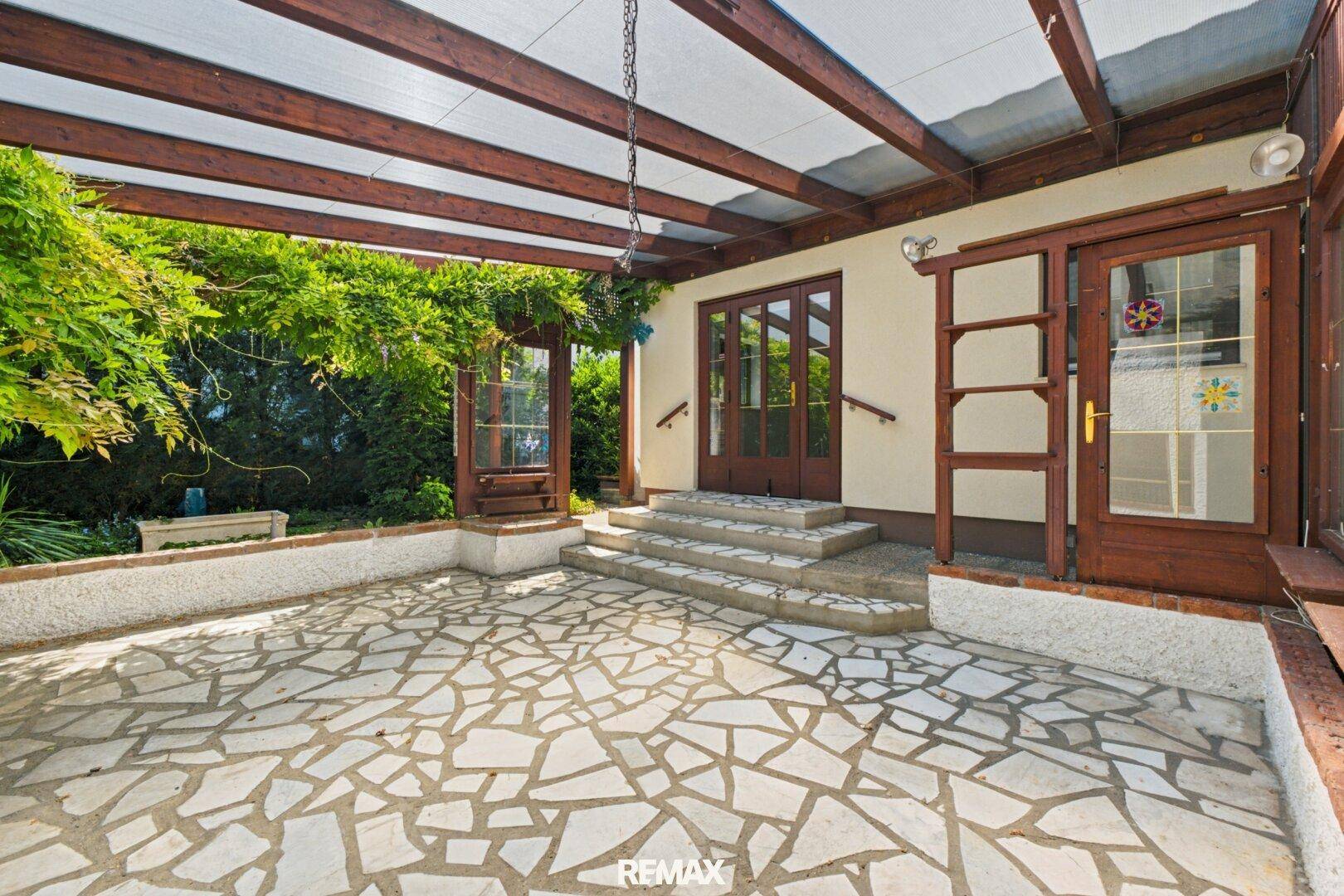 Überdachte Terrasse mit Mosaikboden und üppiger Begrünung, ideal für entspannte Stunden im Freien.