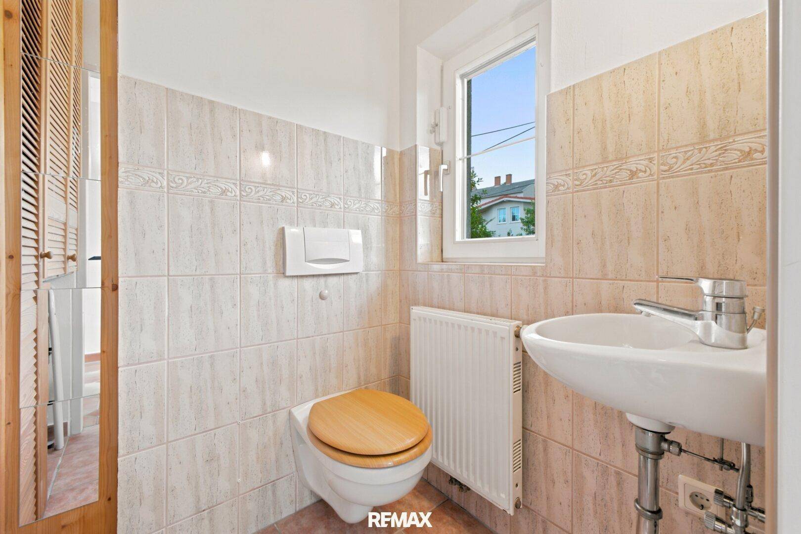 Kleines Gäste-WC mit Fenster, Waschtisch und Wand-WC, in hellem Fliesendesign.