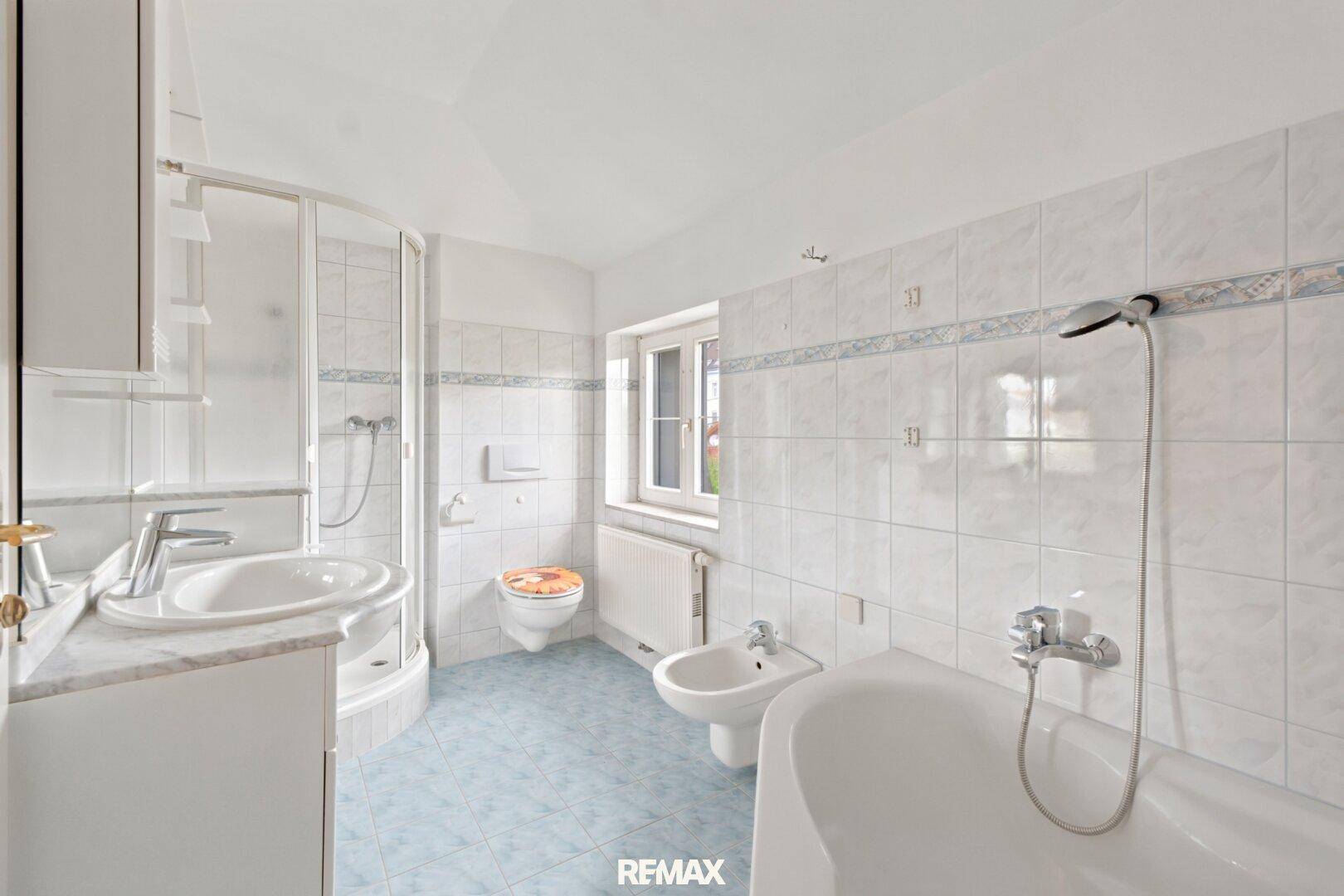 Gefliestes Badezimmer mit Badewanne, Dusche, Bidet und Fenster für natürliche Belüftung.