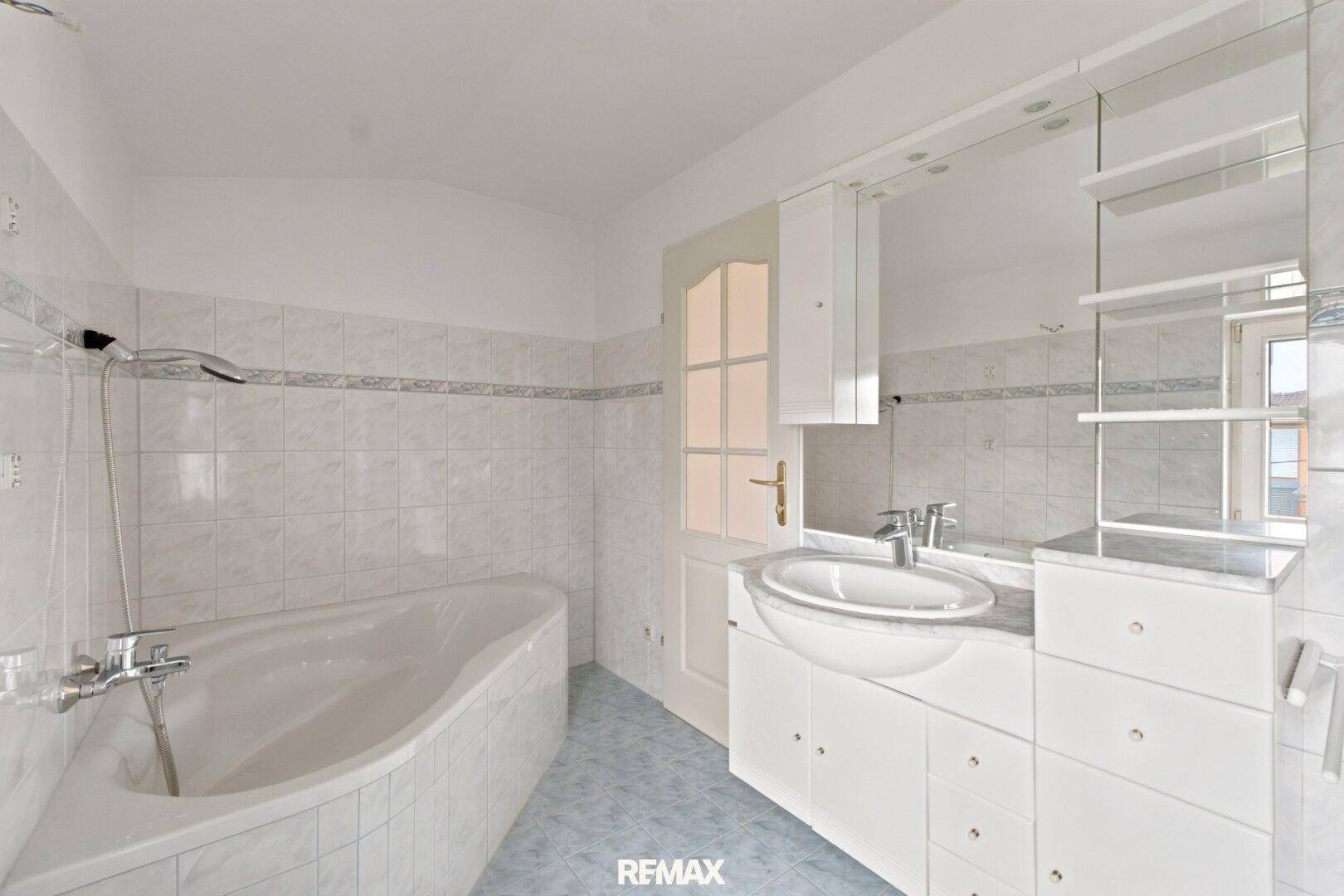 Helles Badezimmer mit Badewanne, Waschtisch und Spiegelschrank, in einem gepflegten Zustand.