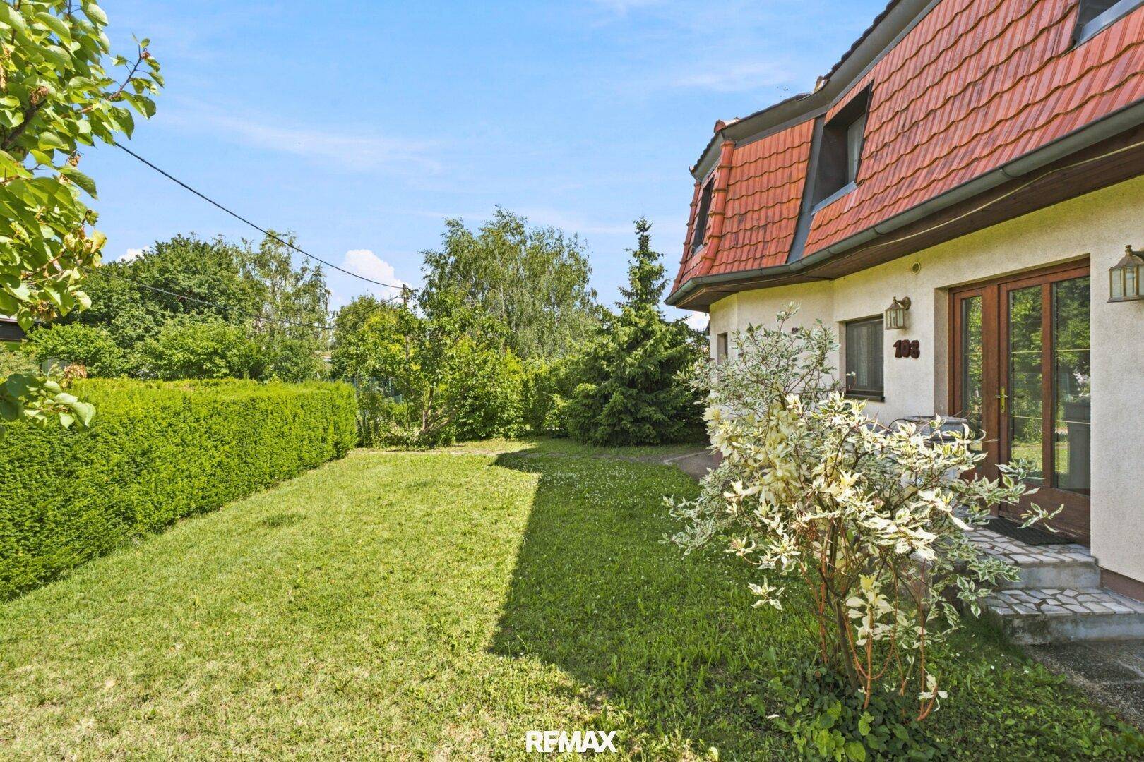 Gepflegter Gartenbereich mit Rasenfläche und Hecke, umgeben von viel Grün.