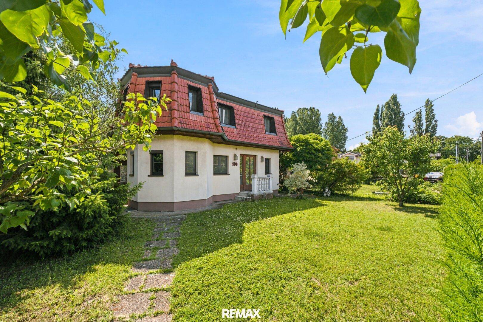 Charmantes Haus mit rotem Ziegeldach und gepflegtem Garten unter blauem Himmel.