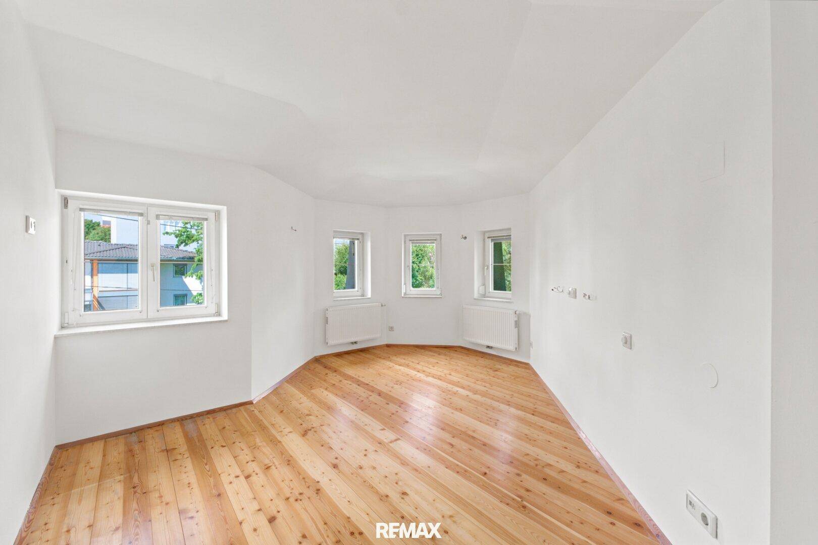 Helles Schlafzimmer mit Holzdielenboden und mehreren Fenstern, die viel Tageslicht hereinlassen.