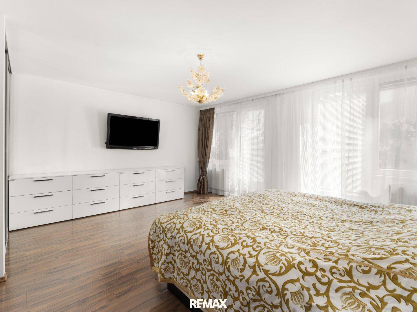 Helles Schlafzimmer mit großem Bett, TV und weißen Kommoden, ausgestattet mit elegantem Holzboden.