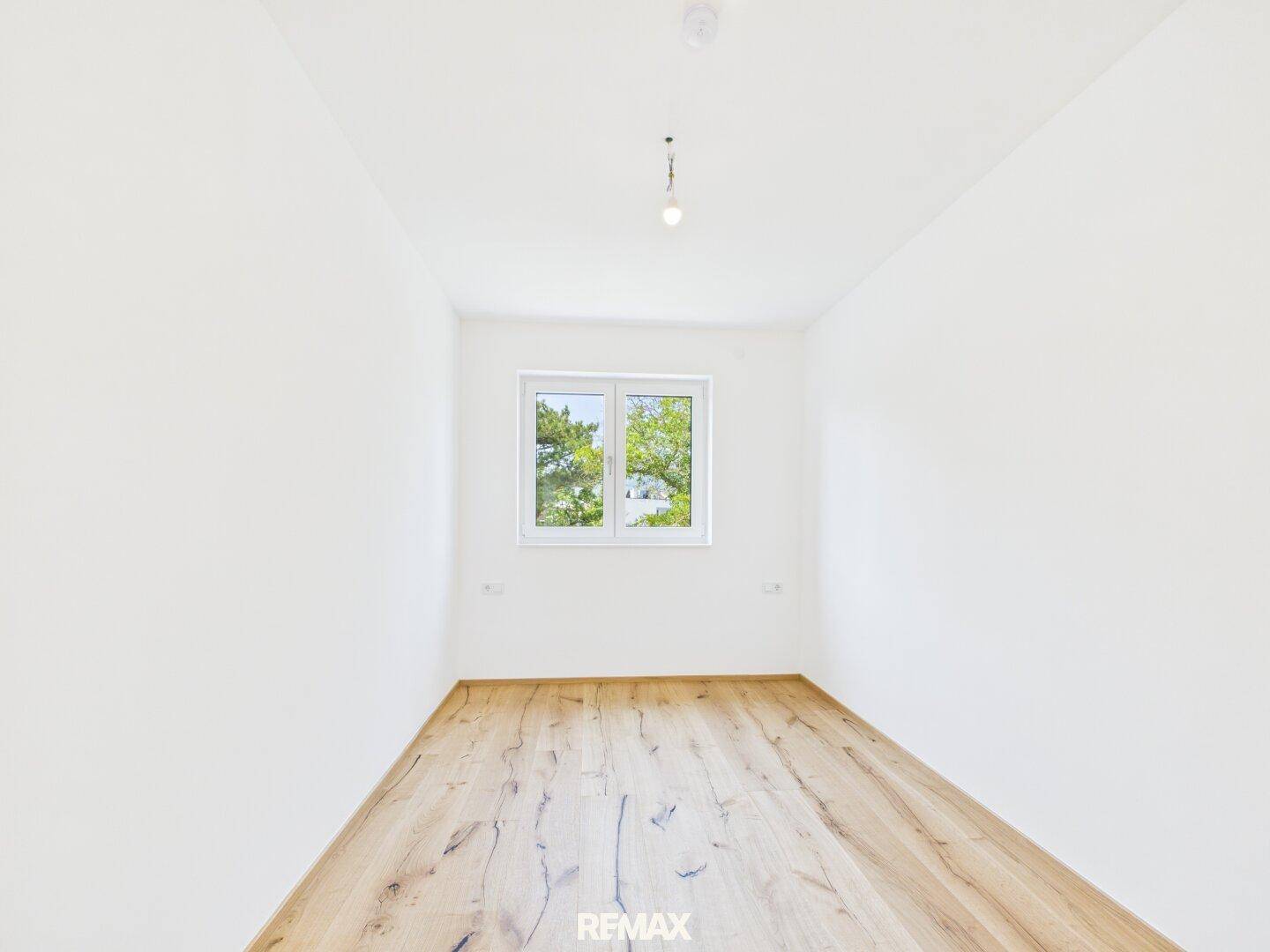 Helles Schlafzimmer mit Holzboden, weißen Wänden und einem Fenster für natürliche Belichtung.