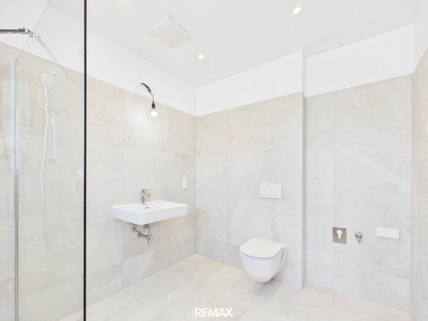 Helles Badezimmer mit wandhängendem WC, modernem Waschbecken und ebenerdiger Dusche.