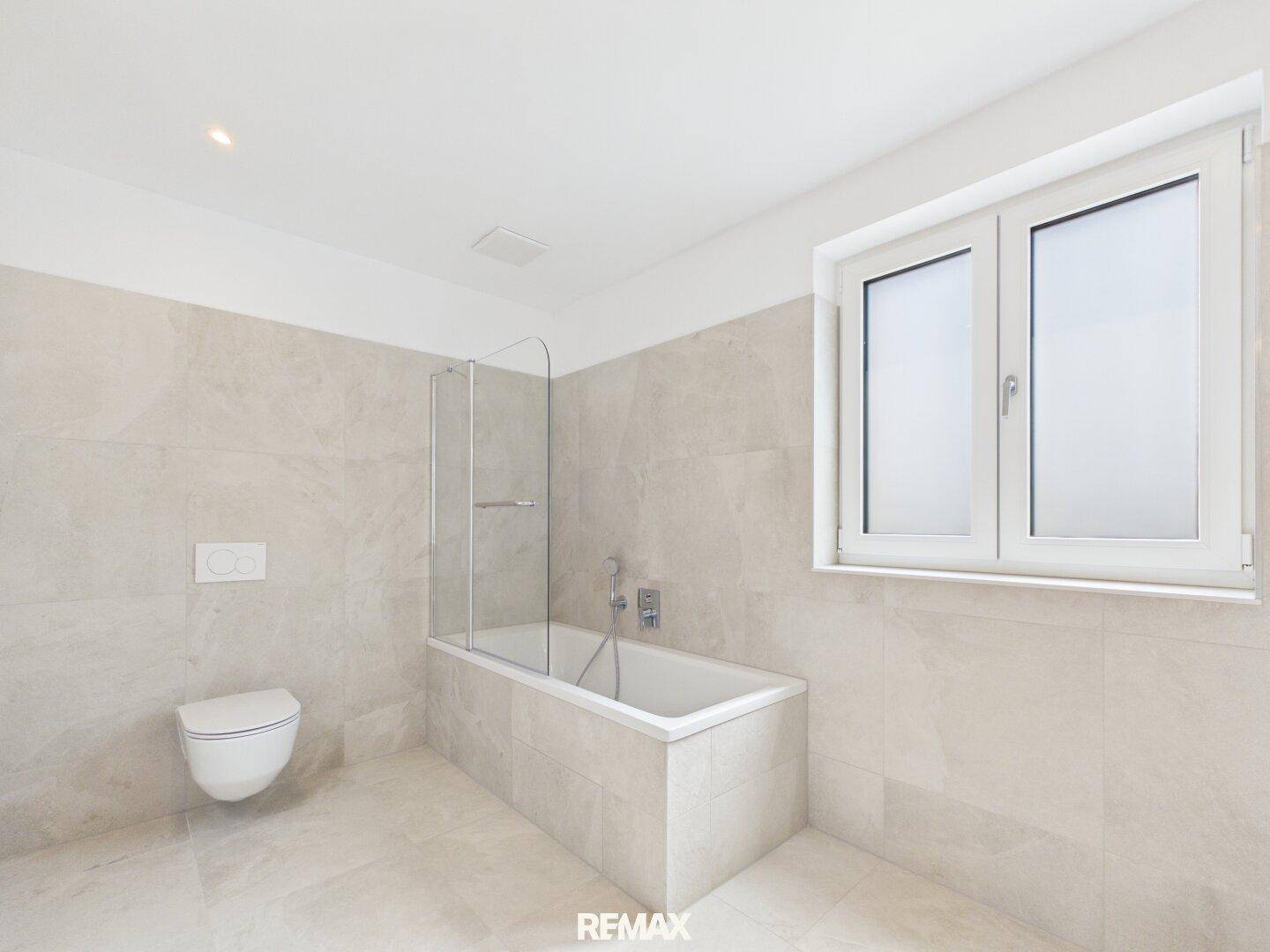 Modernes Badezimmer mit Badewanne, Duschabtrennung, wandhängendem WC und Fenster.