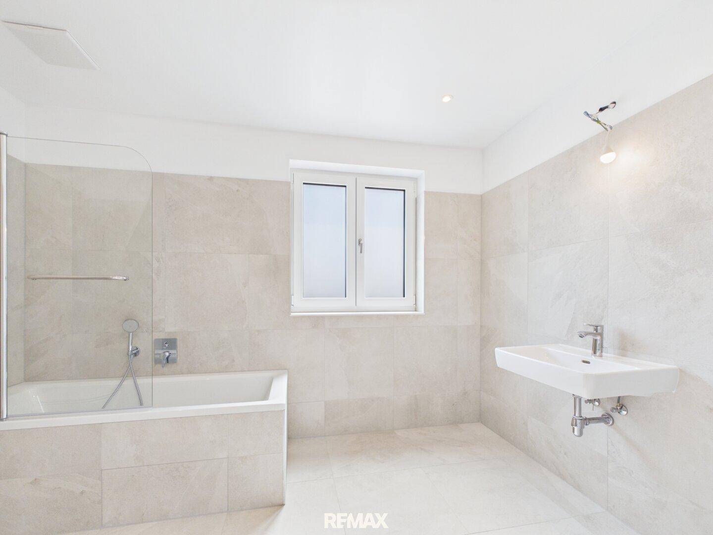 Helles Badezimmer mit Badewanne, modernem Waschbecken und Fenster für Tageslicht.