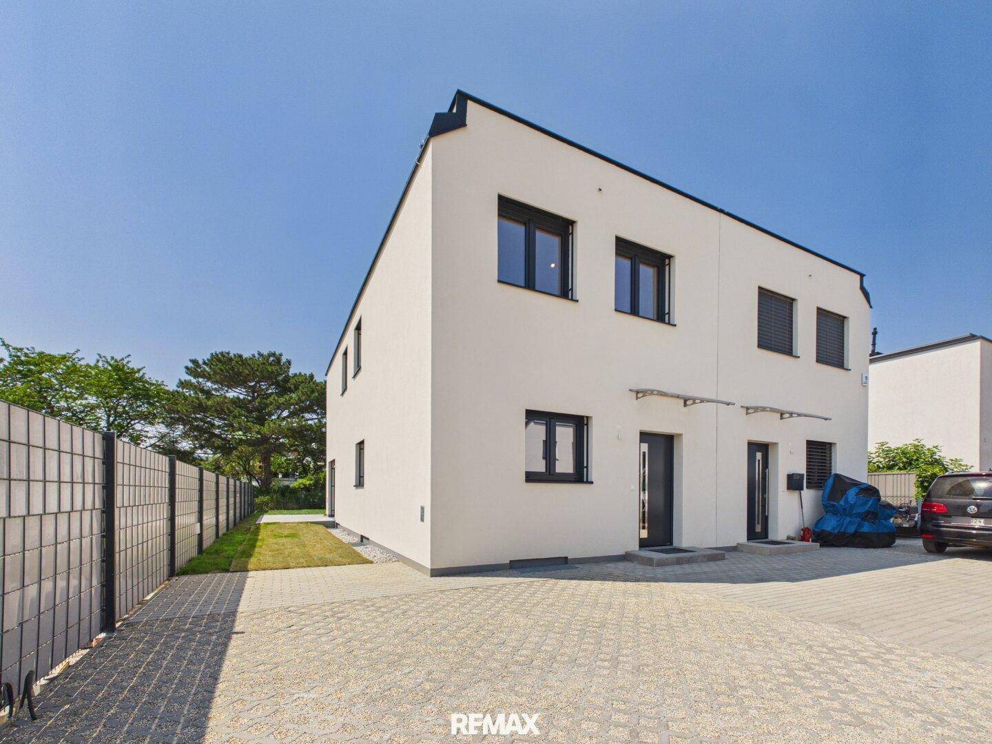 Vorderansicht eines modernen Doppelhauses mit gepflastertem Vorplatz und Parkmöglichkeiten.