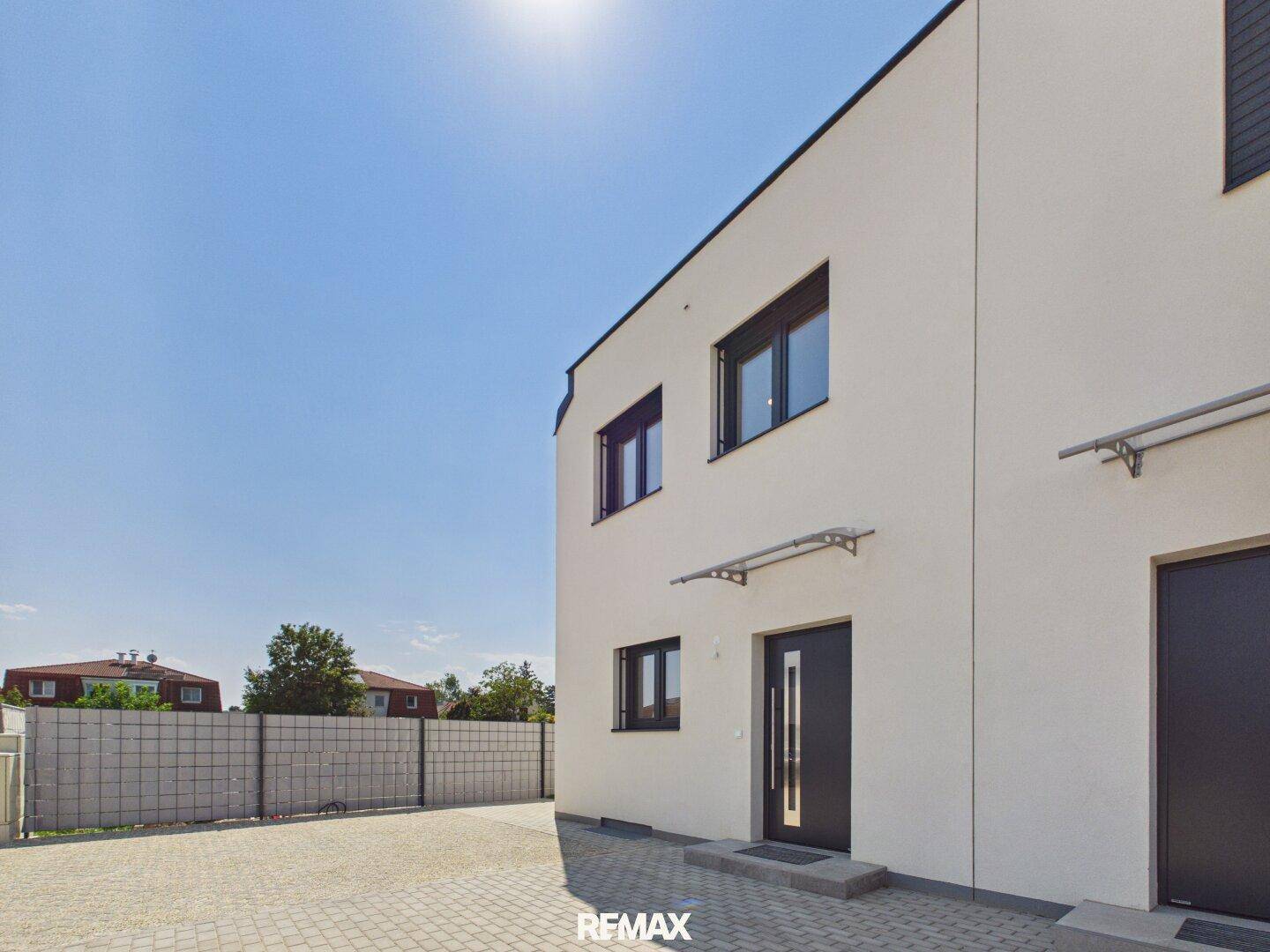 Eingangsbereich eines modernen Hauses mit dunkler Haustür und gepflastertem Zugangsweg.