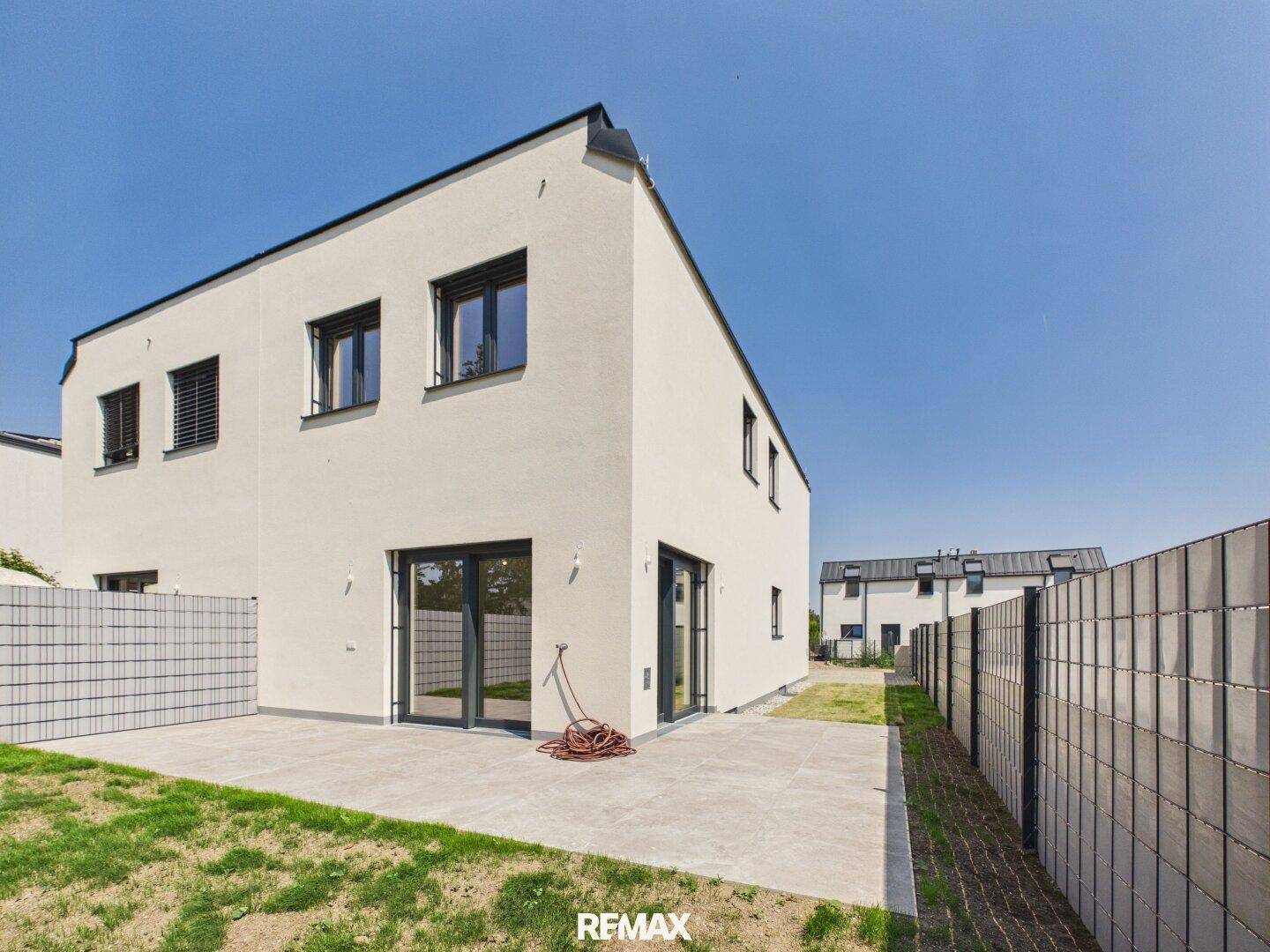 Rückseite des modernen Hauses mit großzügiger Terrasse und angrenzender Rasenfläche.